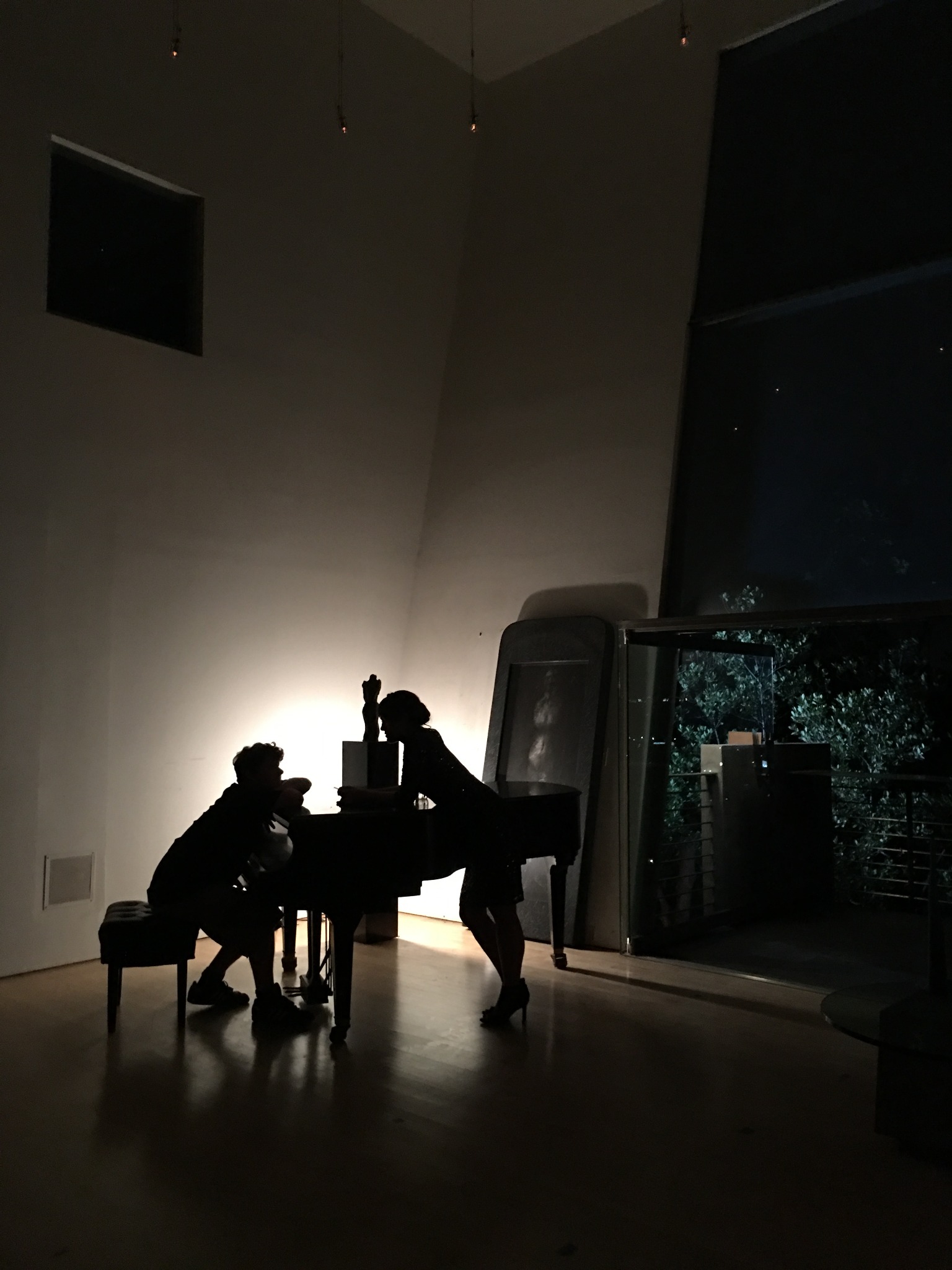 Silhouetted figures beside a piano in a dimly lit room